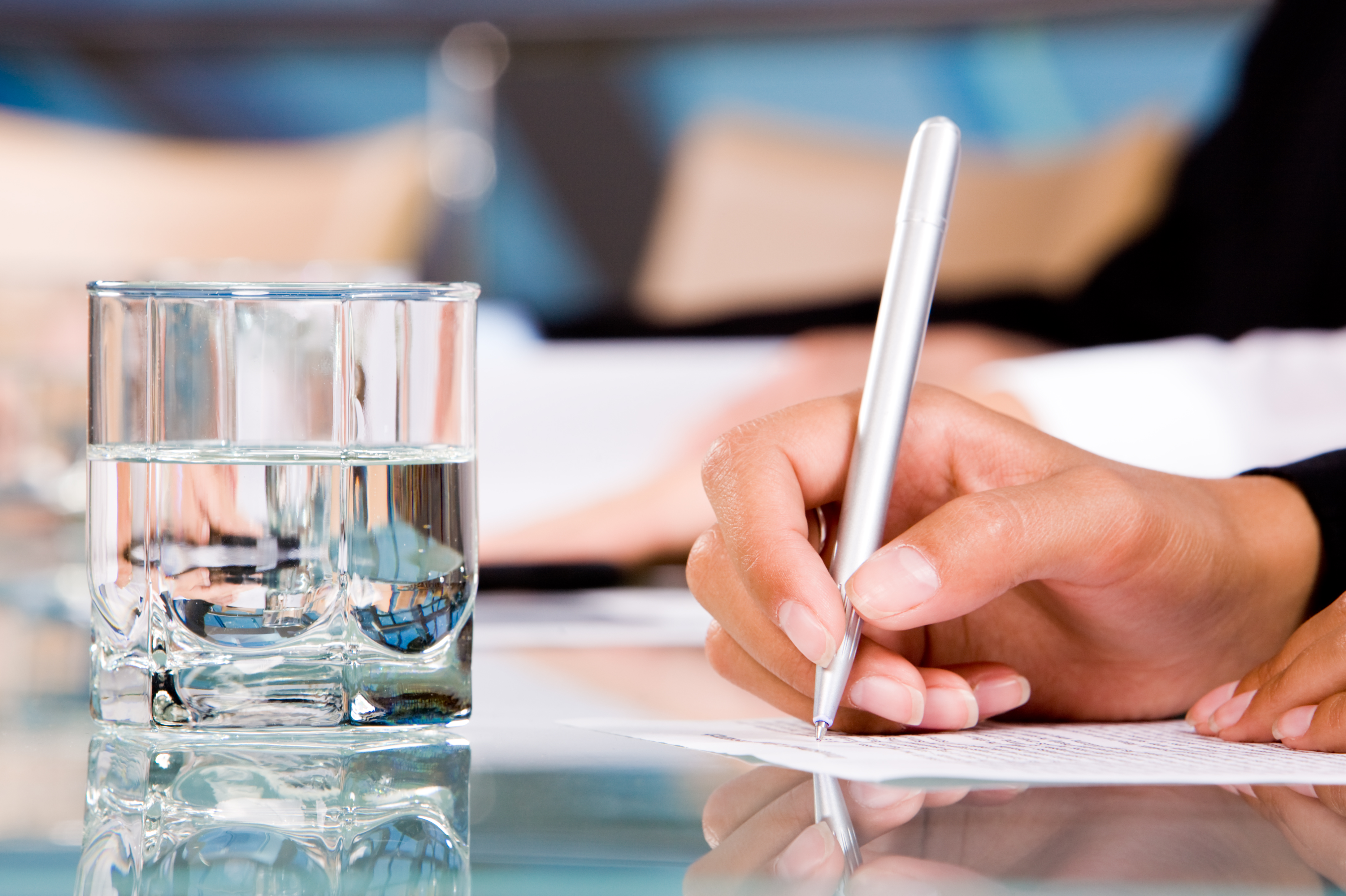 Hånd skriver på papir med et glas vand i forgrunden