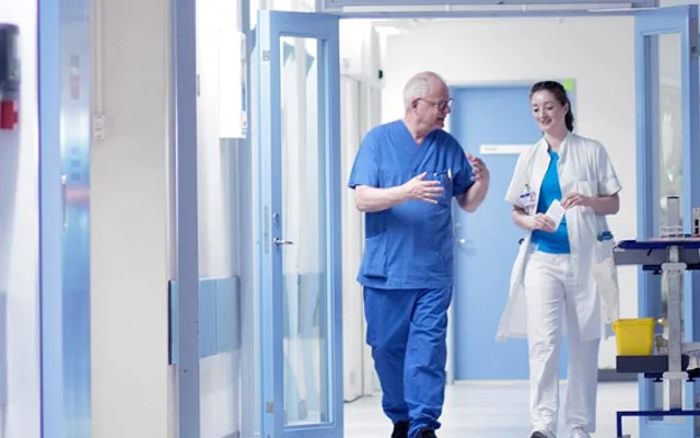 To læger der går ned af en hospitalsgang og har gang i en energisk snak