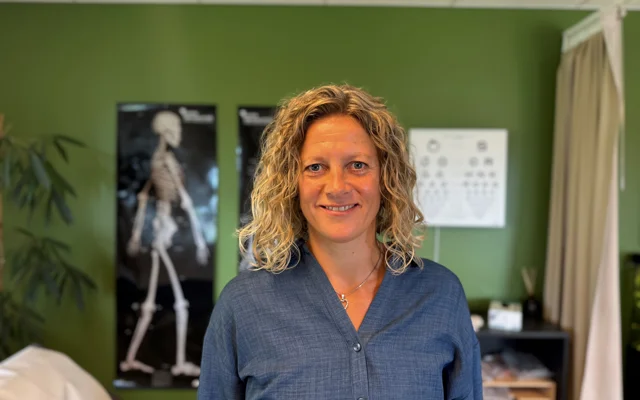 Eva Hvolbæk med løsthængende hår og blå skjorte i en lægeklinik