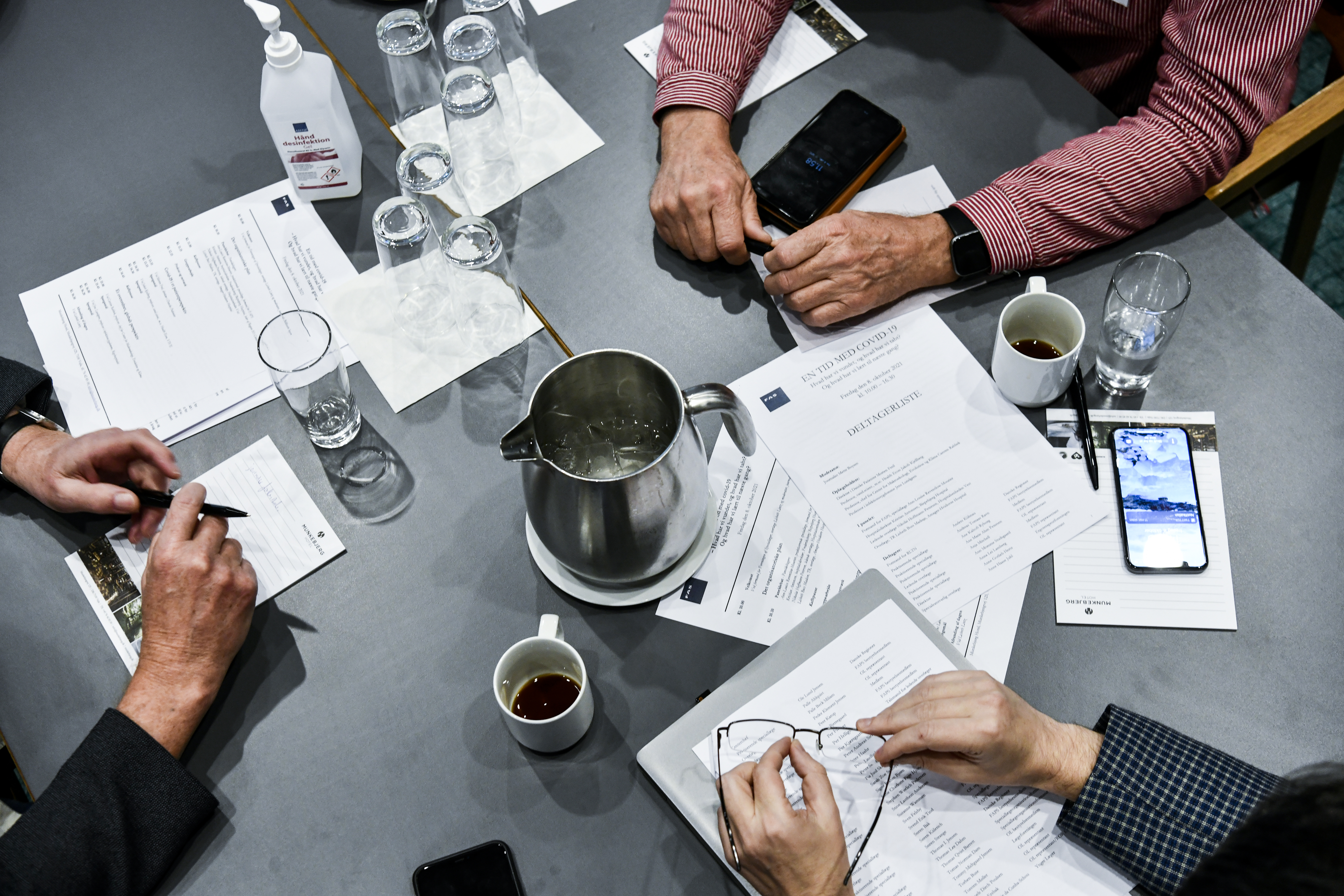 Tre mennesker sidder til møde ved et bord med mange dokumenter