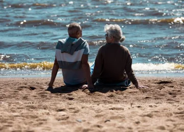 To ældre personer der sidder på stranden og kigger ud over vandet - pension